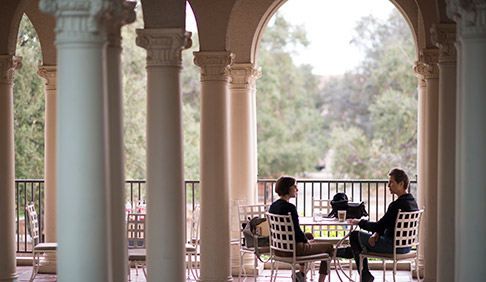Two figures sit on the Branca patio at JSC framed by columns on either side