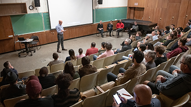 A professor stands in front of a large group of students in a lecture hall